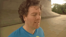 a man with curly hair wearing a blue shirt with a yellow ball on it