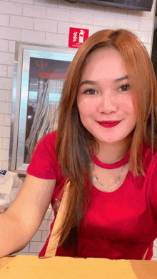 a woman in a red shirt is smiling in front of a fire extinguisher on the wall