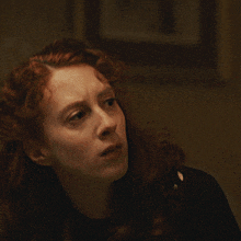 a woman with red hair wearing a black shirt and a necklace