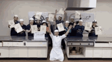 a group of people are posing for a picture in a kitchen while holding up certificates .