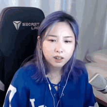 a woman with purple hair is wearing headphones and a blue shirt while sitting in a chair .