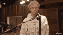 a man in a white hoodie is singing into a microphone in a recording studio .