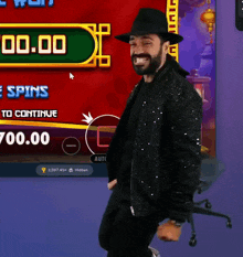 a man in a black jacket and hat stands in front of a screen that says 00.00
