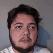 a man with a beard and a white shirt is looking at the camera