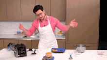 a man in a pink shirt and white apron is standing in front of a vitamix blender
