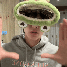 a person wearing a frog hat and a grey hoodie that says welcome