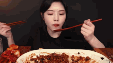 a woman is eating food with chopsticks and a spoon