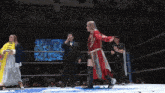 a woman in a red robe stands in a wrestling ring next to a referee
