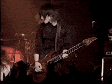 a man in a black shirt is playing a red electric guitar on a stage .