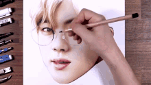 a person is drawing a portrait of a young man wearing glasses