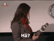 a woman holds a piece of metal in front of a wall clock and says " ha "