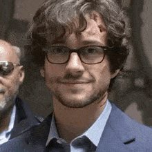 a close up of a man wearing glasses and a suit smiling .