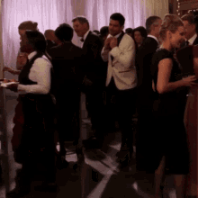 a man in a white tuxedo is adjusting his tie