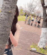a woman peeking out from behind a tree with a group of people behind her