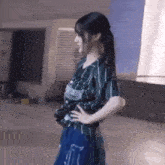 a woman in a striped shirt and blue skirt is standing on a sidewalk with her hands on her hips .