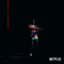 a man in a red white and blue striped shirt is standing in the dark with a netflix logo behind him