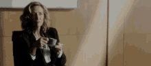 a woman in a suit is drinking a cup of coffee while sitting in a chair .