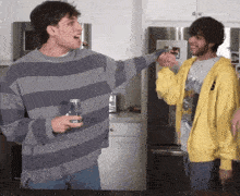 a man in a striped sweater holds a can of soda next to another man in a yellow hoodie