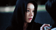 a woman wearing a black hoodie is looking at another person .