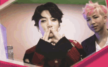 a man with pink hair is standing next to a man with black hair making a heart with his hands .