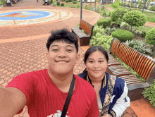 a man and a woman pose for a picture in front of a park