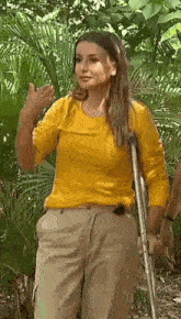 a woman in a yellow shirt and khaki pants is standing in the jungle with crutches .