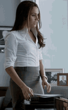 a woman in a white shirt and gray skirt is standing in front of a stack of papers