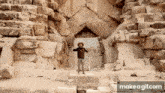 a man in a cowboy hat is standing in front of a large rock wall .
