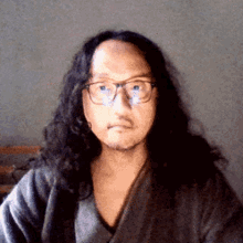 a man with long hair and glasses is wearing a gray robe