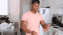 a man in a pink shirt and black hat stands in front of a white refrigerator