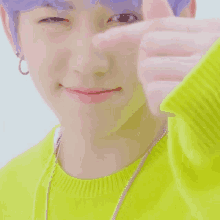 a close up of a person with purple hair making a heart shape with their finger