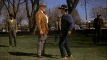 a man in a cowboy hat is standing next to another man in a park .