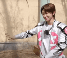 a young man in a pink and white jacket with a gopro on his neck is standing in front of a wall .