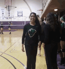 a girl wearing a black shirt with a green buffalo on it stands on a basketball court