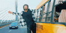 a man in a plaid shirt is standing next to a yellow school bus .