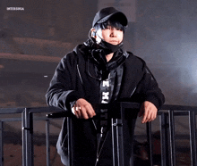 a man wearing a mask and headphones stands next to a fence with the words intersuga written on the bottom