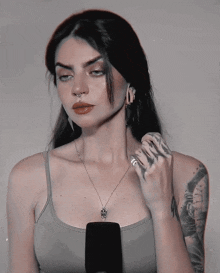 a woman with a tattoo on her arm is wearing a tank top and a necklace