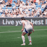 a female soccer player stands on the field in front of a live your best sign
