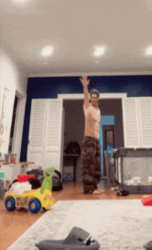 a man without a shirt is dancing in a living room with a toy car in the foreground