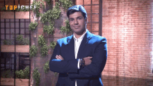 a man in a blue suit stands with his arms crossed in front of a brick wall with the word top chef on it