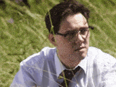 a man wearing glasses and a tie is sitting in a field of tall grass