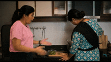 a woman in a pink shirt is talking to another woman in a blue and white dress