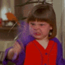 a little girl in a red shirt and purple jacket is brushing her teeth with a toothbrush