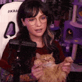 a woman is holding a cat in front of a white akra chair