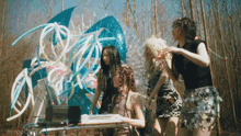a group of women are standing around a table in a forest looking at a laptop .