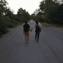 two people walking down a road holding hands with trees in the background