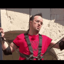 a man wearing a red shirt and a harness is standing in front of a wall .