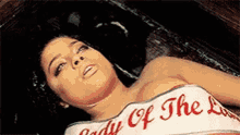 a woman is laying in a coffin wearing a white top that says lady of the lake