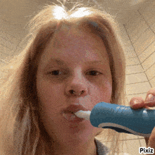 a woman is brushing her teeth with a blue toothbrush and a pixiz watermark on the bottom