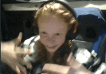 a girl with red hair wearing headphones is smiling and giving a thumbs up